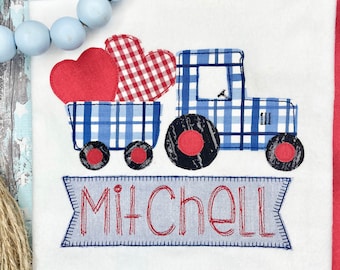 May include: A blue and white plaid tractor carrying two red hearts, one with a red and white plaid pattern. The tractor has black wheels and a red and black tire. A blue banner with the name "Mitchell" is below the tractor.