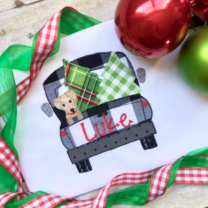 May include: A white t-shirt with a black and white checkered truck carrying a green and red plaid Christmas tree and a yellow dog. The truck has the name "Luke" embroidered on the back.