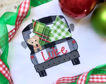 May include: A white t-shirt with a black and white checkered truck carrying a green and red plaid Christmas tree and a yellow dog. The truck has the name "Luke" embroidered on the back.