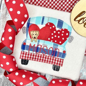 May include: Embroidered design of a red and blue pickup truck with a dog and two hearts in the bed. The truck has a red and white checkered pattern on the back and the name "Mason" is embroidered on the side.