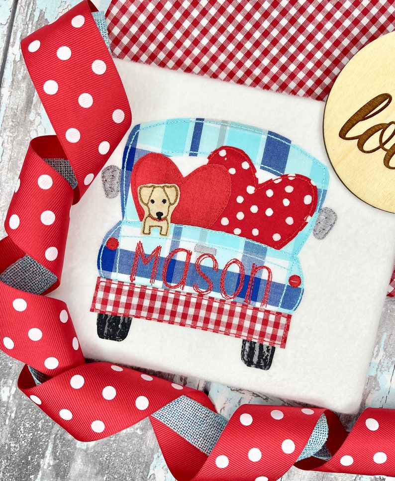 May include: Embroidered design of a red and blue pickup truck with a dog and two hearts in the bed. The truck has a red and white checkered pattern on the back and the name "Mason" is embroidered on the side.
