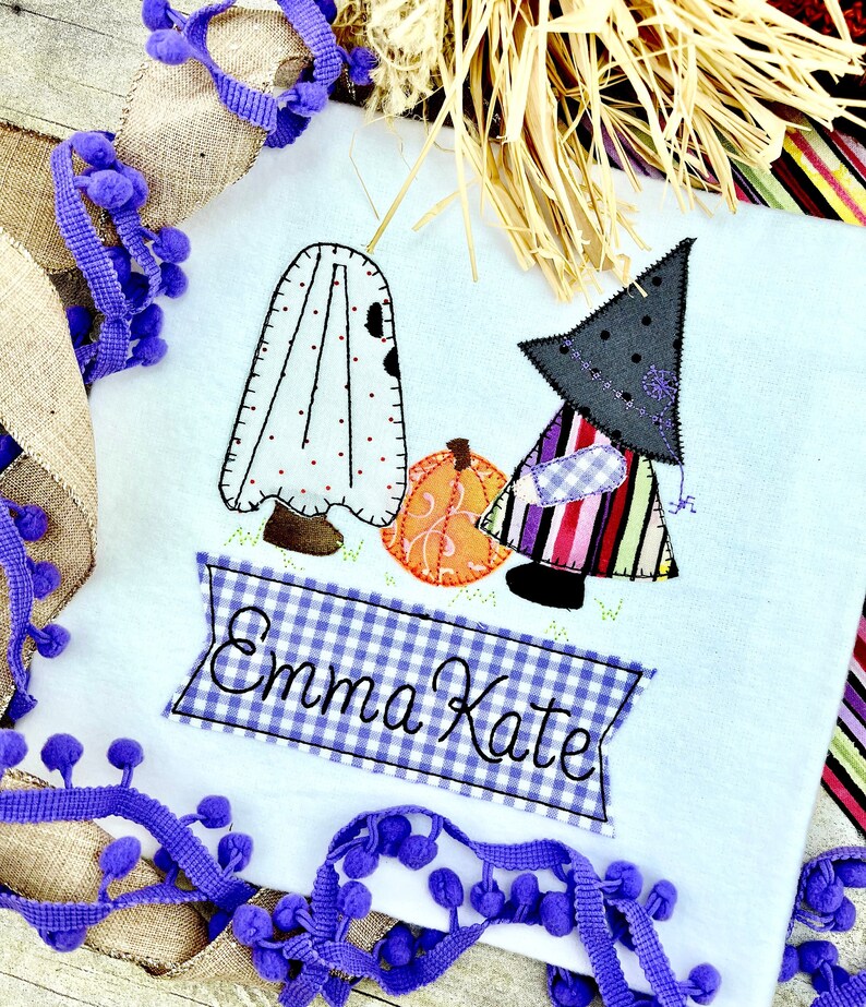 May include: A white fabric appliqu&eacute; of a ghost and a witch holding a pumpkin with a blue and white checkered banner that reads "Emma Kate".