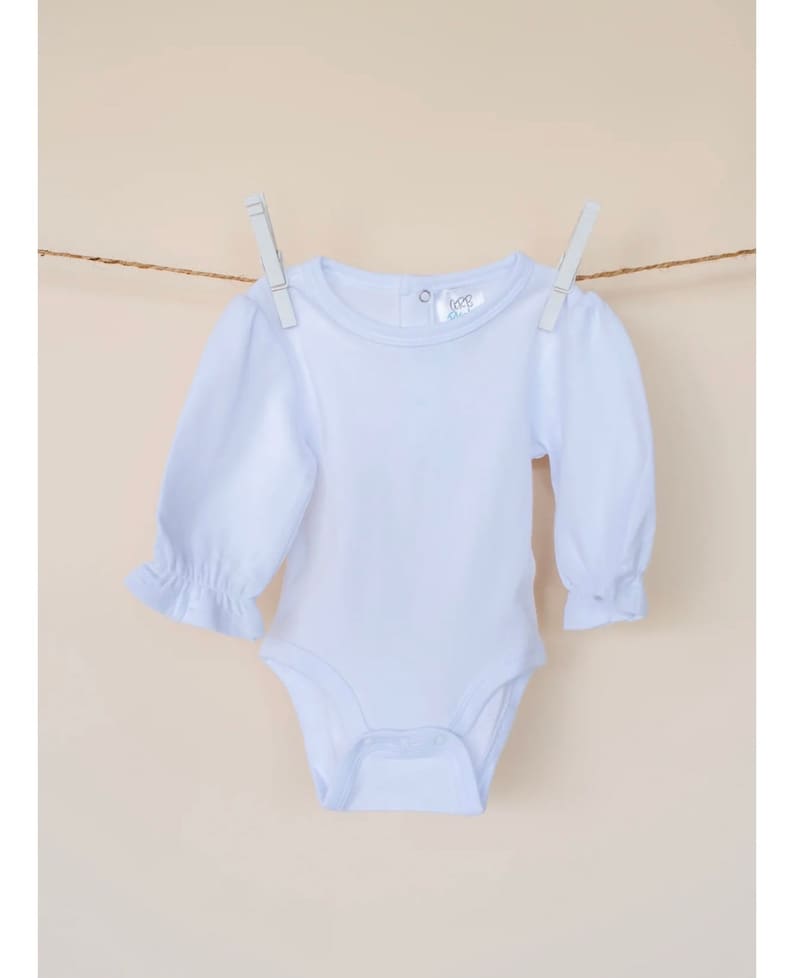 May include: A white long-sleeved baby bodysuit with a ruffled sleeve detail. The bodysuit has a round neckline and a snap closure at the crotch.