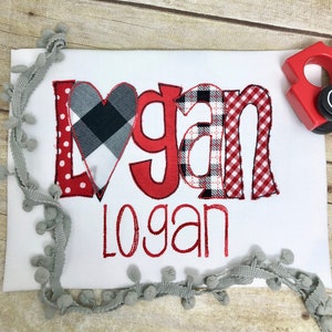 May include: Red and black checked fabric heart with the name "Logan" spelled out in red fabric letters with a red and white checked fabric background. The name "Logan" is also spelled out in red cursive below the letters.