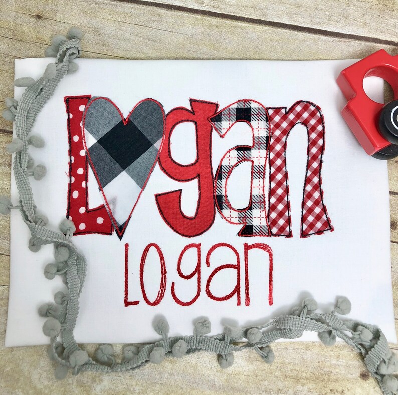 May include: Red and black checked fabric heart with the name "Logan" spelled out in red fabric letters with a red and white checked fabric background. The name "Logan" is also spelled out in red cursive below the letters.