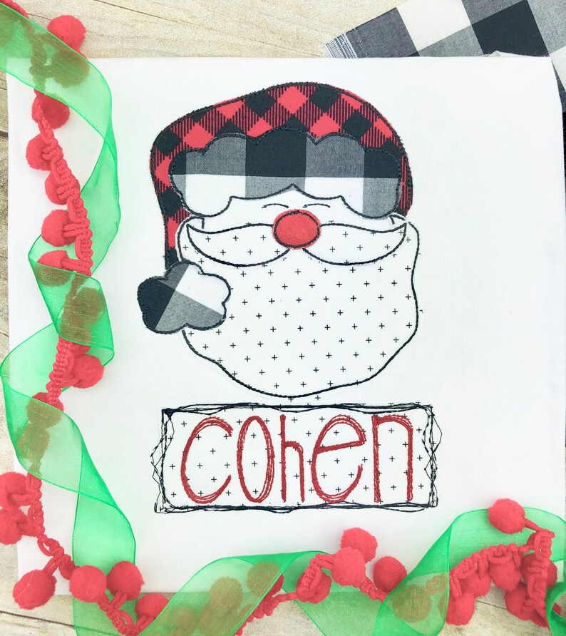 May include: White square with a Santa Claus design. The Santa's hat is red and black buffalo plaid, with a matching cuff. The beard is white with small black crosses. The name "COHEN" is in red.