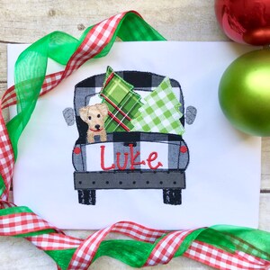 May include: A black and white checkered pickup truck with a green and white plaid Christmas tree and a green and white checkered Christmas tree in the back. A small brown dog is peeking out of the truck bed. The truck has the name "Luke" written on the back.