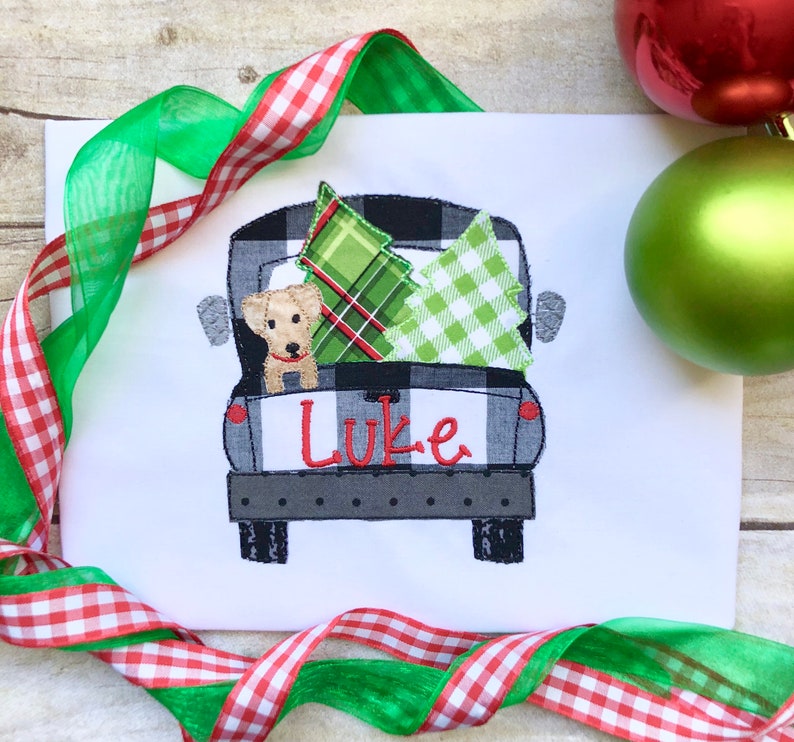 May include: A black and white checkered pickup truck with a green and white plaid Christmas tree and a green and white checkered Christmas tree in the back. A small brown dog is peeking out of the truck bed. The truck has the name "Luke" written on the back.