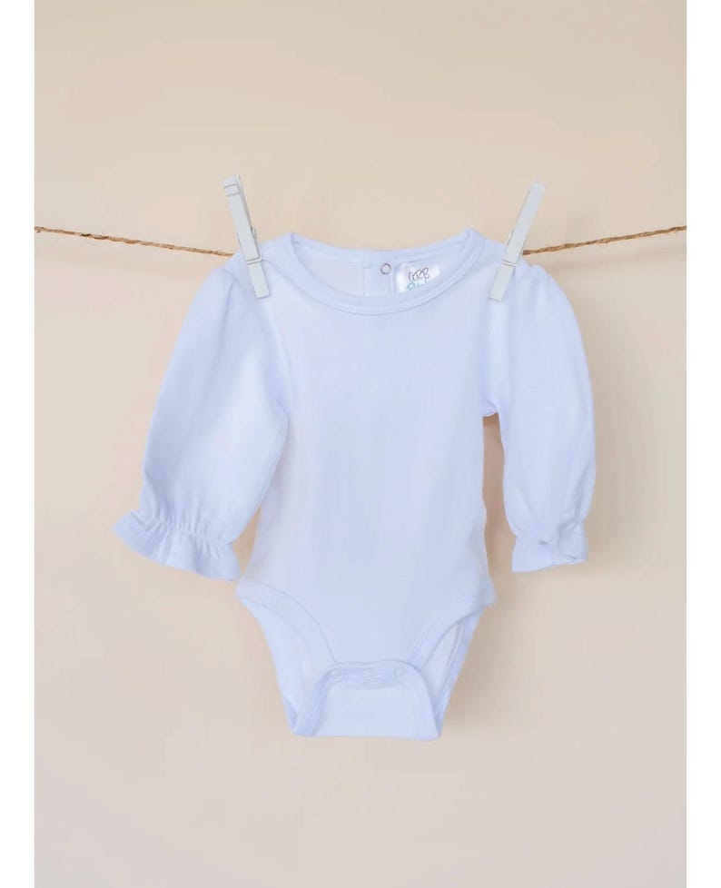 Pu&ograve; includere: Un body bianco a maniche lunghe per neonato con scollo rotondo e maniche a sbuffo. Il body ha una chiusura a pressione nella parte inferiore.