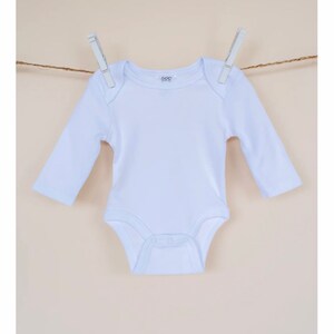 May include: A white long-sleeved baby onesie hanging on a clothesline with two clothespins. The onesie has a small logo on the front that says "6-12M".