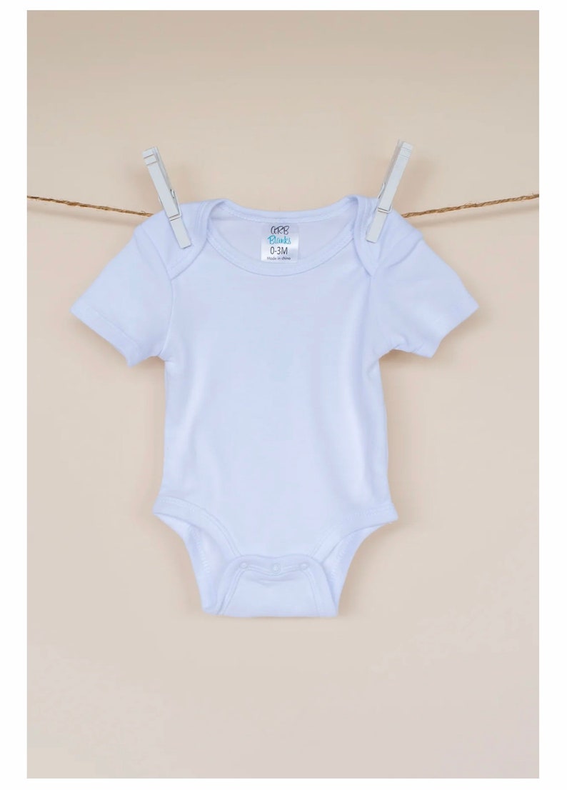 May include: White baby onesie with short sleeves and snaps at the bottom. The onesie has a label that says "CCB Blanks 0-3M Made in China".