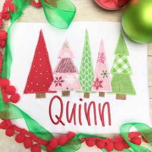 Puede incluir: Un pelele blanco con cinco &aacute;rboles de Navidad de patchwork coloridos y el nombre "Quinn" bordado en rojo.