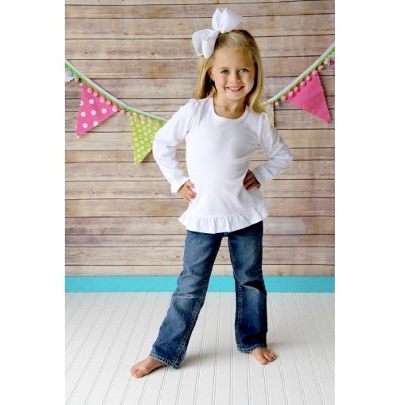 Puede incluir: Una camisa blanca de manga larga con un dobladillo con volantes, usada con jeans azules y un lazo blanco.