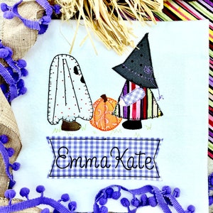 May include: A white fabric ghost and a witch with a black hat and striped dress stand next to a pumpkin. A blue and white gingham banner reads "Emma Kate".