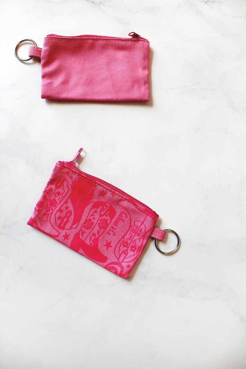 May include: Two pink zippered pouches with key rings. The top pouch is plain and the bottom pouch has a pink floral design.