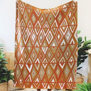 May include: A large throw blanket with a geometric pattern in shades of orange, brown, and white. The blanket features a repeating diamond pattern.