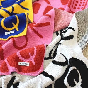 May include: A collection of colorful knitted blankets with different patterns and designs. The blankets are made of soft, cozy yarn and feature bold, graphic prints. Each blanket has a label with the text "Calhoun & Co."