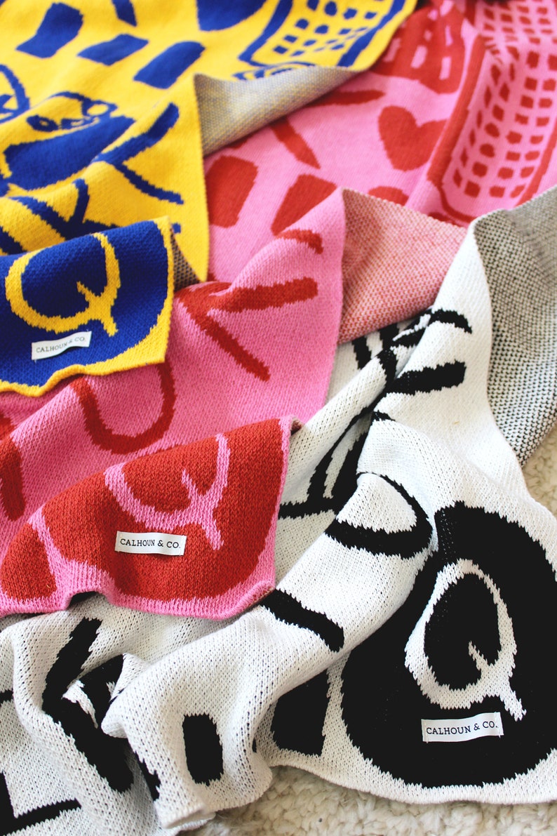 May include: A collection of colorful knitted blankets with different patterns and designs. The blankets are made of soft, cozy yarn and feature bold, graphic prints. Each blanket has a label with the text "Calhoun & Co."