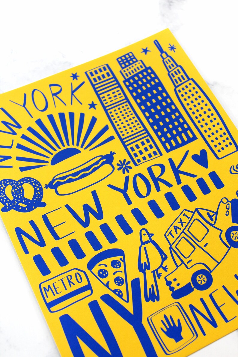 May include: A yellow background with blue illustrations of New York City landmarks, including the Empire State Building, a hot dog, a pretzel, a slice of pizza, a taxi cab, and the words "New York" and "Metro".