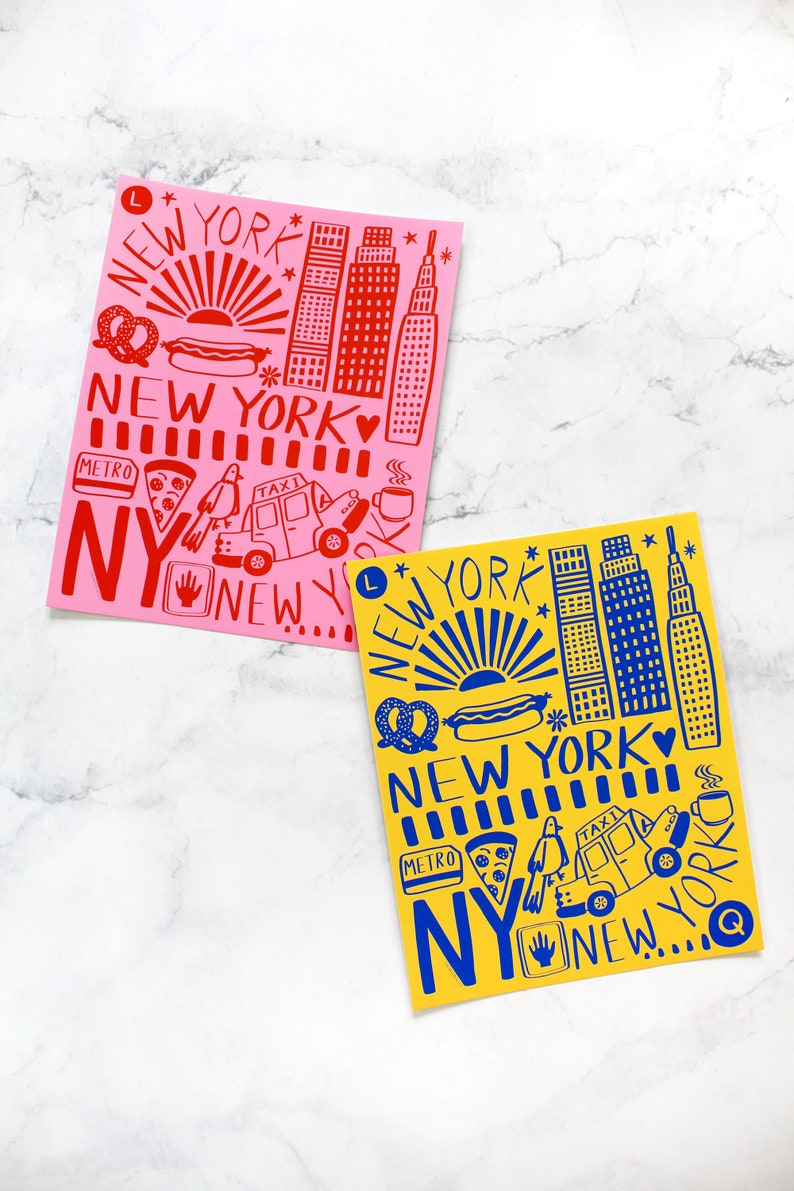 May include: Two illustrated prints of New York City landmarks, one in red on a pink background and one in blue on a yellow background. Both prints feature the text "New York" and include iconic symbols like the Empire State Building, hot dogs, pretzels, and taxis.