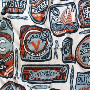 May include: A colorful patterned fabric with a repeating design of sardine cans. The cans are in various colors, including blue, orange, and red, and feature different text, such as "Ocean Fresh Sardines" and "Very Good".