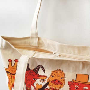 May include: A beige canvas tote bag with a zipper closure. The bag features a colorful print of various animals, including a giraffe, a goat, an ostrich, and a bear.