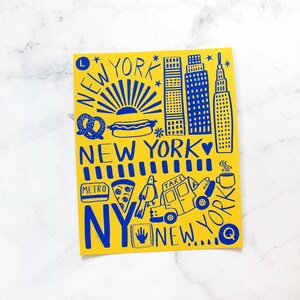 May include: A yellow card with blue illustrations of New York City landmarks, food, and transportation. The text "NEW YORK" appears multiple times on the card.