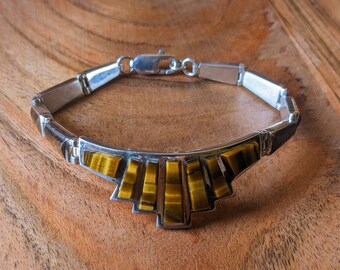 May include: A silver bracelet with a geometric design featuring tiger's eye stones. The stones are a mix of brown and gold.