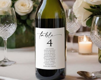 May include: A white wine bottle with a white label that says "table 4" and lists a number of names. The bottle is sitting on a white tablecloth with a white candle and two wine glasses.