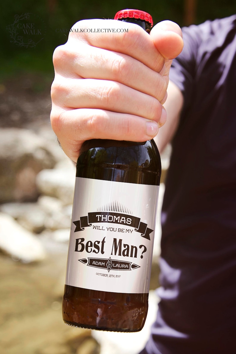 May include: A brown glass bottle with a white label that says "Thomas Will You Be My Best Man? Adam & Laura October 12th, 2017".