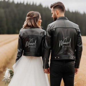Könnte beinhalten: Ein Paar trägt schwarze Lederjacken mit dem Schriftzug "Just Married" auf dem Rücken. Die Braut trägt ein weißes Hochzeitskleid und der Bräutigam trägt eine schwarze Hose. Das Paar steht auf einem Feld.