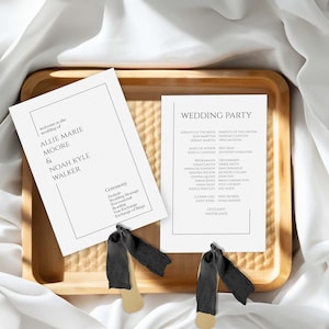 May include: A black and white wedding program with a black ribbon. The program lists the wedding ceremony order and the wedding party.