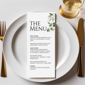 Peut inclure: Une carte de menu blanche avec le texte "THE MENU" et une liste de plats, dont la salade de tomates héritage et burrata et la poitrine de poulet aux herbes. La carte est sur une assiette blanche avec des couverts dorés et un verre de liquide.