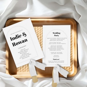 Puede incluir: Dos tarjetas blancas con texto negro. La tarjeta superior dice "Bienvenido a la boda de Indie & Rowan" y enumera el orden de la ceremonia. La tarjeta inferior dice "Wedding Party" y enumera los nombres de los miembros de la fiesta de bodas.