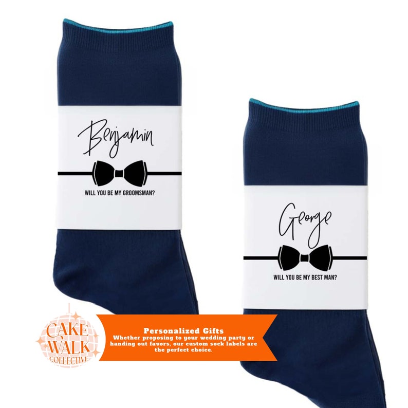 Pu&ograve; includere: Due paia di calzini blu navy con etichette bianche. Le etichette hanno un papillon nero e il testo "Vuoi essere il mio testimone?" e "Vuoi essere il mio testimone d'onore?" con i nomi "Benjamin" e "George" scritti in corsivo.