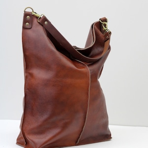 May include: A large brown leather tote bag with a long strap and a gold buckle. The bag has a slouchy, casual look.