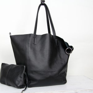 May include: A black leather tote bag with a smaller matching pouch. The tote bag has a single top handle and a silver ring detail.