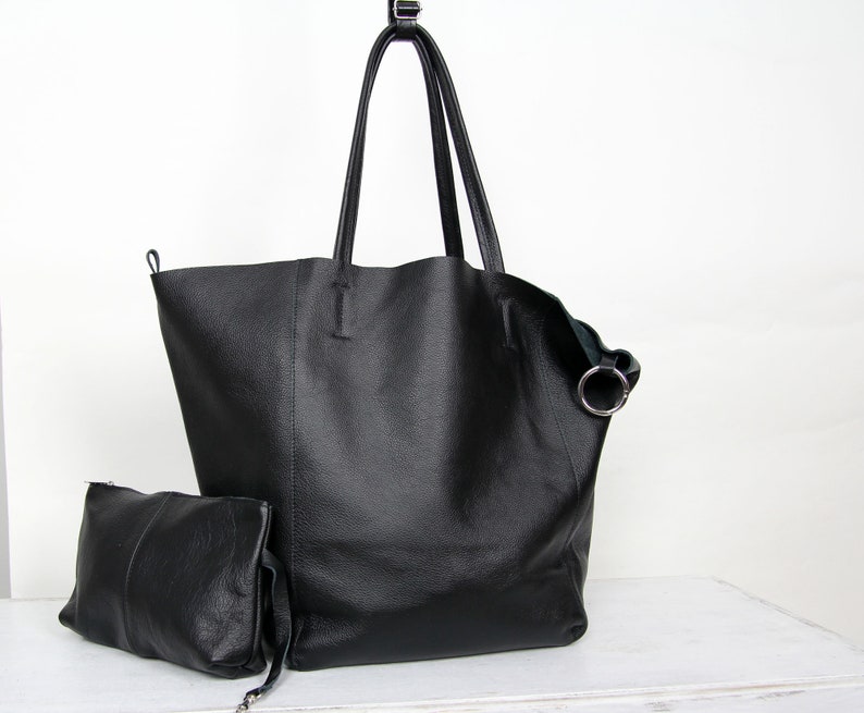 May include: A black leather tote bag with a smaller matching pouch. The tote bag has a single top handle and a silver ring detail.
