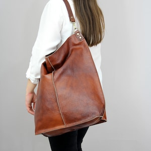 May include: A large brown leather tote bag with a long strap. The bag has a slouchy, casual look and is made of high-quality leather.