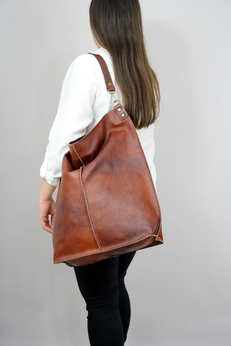 May include: A large brown leather tote bag with a long strap. The bag has a slouchy, casual look and is made of high-quality leather.