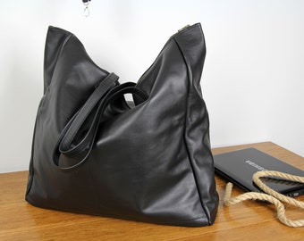 May include: A large black leather tote bag with a zipper closure and two long straps. The bag is sitting on a wooden surface.