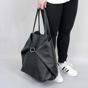 May include: A large black leather tote bag with a silver ring detail. The bag has a slouchy, unstructured shape and is perfect for carrying everyday essentials.