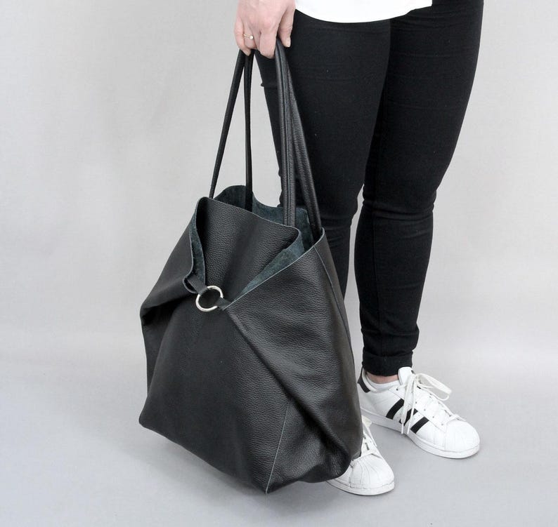 May include: A large black leather tote bag with a silver ring detail. The bag has a slouchy, unstructured shape and is perfect for carrying everyday essentials.