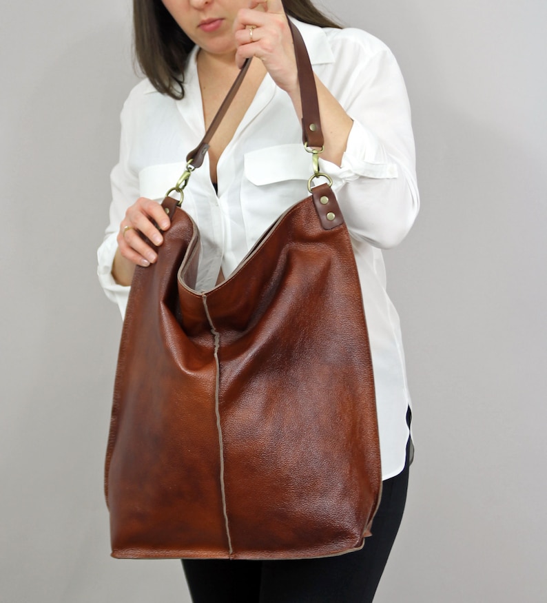 May include: A brown leather tote bag with a long strap. The bag has a slouchy, casual look and is made of a soft, supple leather.