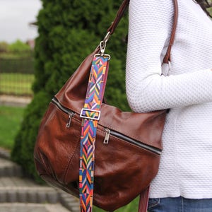 Pu&ograve; includere: Una borsa a tracolla in pelle marrone con una tracolla a fantasia colorata. La borsa ha una chiusura a zip e una patta con chiusura magnetica.