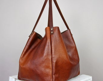 May include: A large brown leather tote bag with two long straps. The bag has a slouchy, unstructured shape and is made of a soft, supple leather.