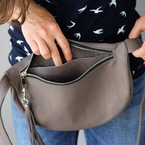 May include: A brown leather fanny pack with a zipper closure and a fringe detail. The bag is open and the inside is visible.