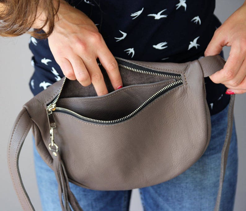 May include: A brown leather fanny pack with a zipper closure and a fringe detail. The bag is open and the inside is visible.