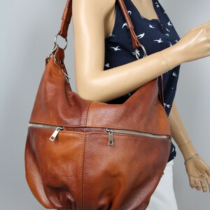 Pu&ograve; includere: Una borsa a tracolla in pelle marrone con una tasca con cerniera e un tiretto della cerniera argentato. La borsa ha un aspetto casual e morbido.