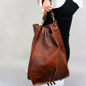 May include: A large brown leather tote bag with a long strap. The bag has a slouchy, relaxed look and is made of high-quality leather.